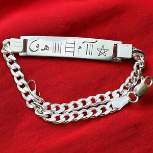 Puede incluir: Una pulsera de plata con un dije rectangular que tiene escritura árabe y un símbolo de estrella. La pulsera está hecha de una cadena de eslabones.