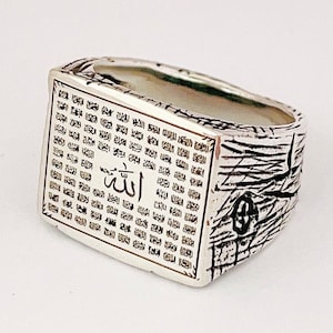 May include: A silver ring with a rectangular design featuring Arabic script and the word "الله" (Allah) in the center. The ring has a textured band.