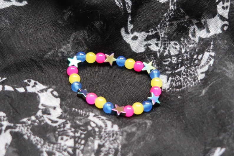 May include: A colorful beaded bracelet with alternating blue, yellow, and pink beads. Each bead has a silver star charm.