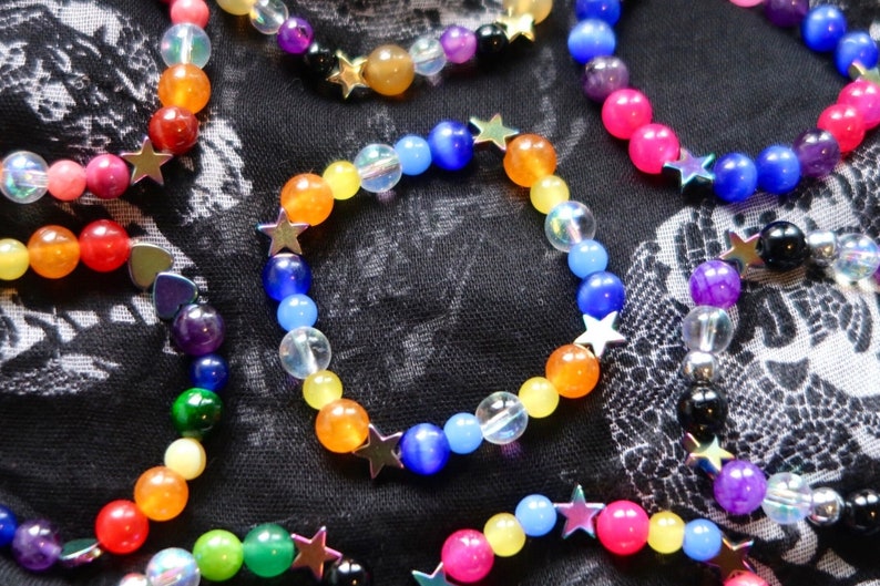 Aroace pride flag star beaded gemstone bracelet. The beads are the aroace flag colors (orange, yellow, white, blues) and holographic stars. The bracelet is surrounded by other LGBTQ pride bracelets.
