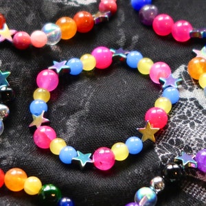 Pansexual/Panromantic pride flag star beaded gemstone bracelet. The beads are the pan flag colors (pink, yellow, cyan) and holographic stars. The bracelet is surrounded by other LGBTQ pride bracelets
