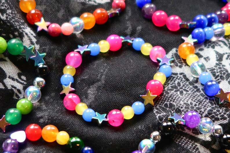 Pansexual/Panromantic pride flag star beaded gemstone bracelet. The beads are the pan flag colors (pink, yellow, cyan) and holographic stars. The bracelet is surrounded by other LGBTQ pride bracelets