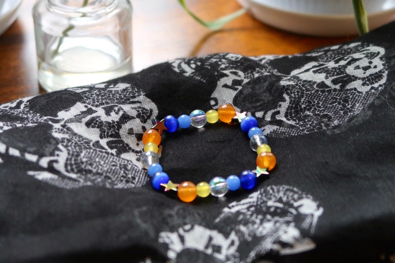 Aroace pride flag star beaded gemstone bracelet. The beads are the aroace flag colors (orange, yellow, white, blues) and holographic stars.