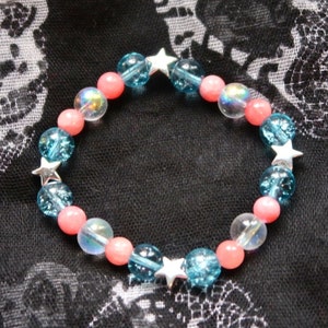 Puede incluir: Un brazalete de cuentas rosa y azul con abalorios de estrella plateados.