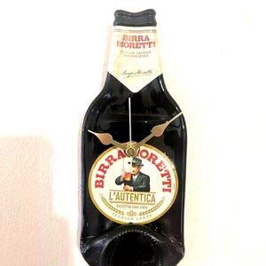 May include: A black beer bottle clock with a gold-colored face and hands. The bottle is labeled with the text "Birra Moretti L'Autentica Ricetta dal 1859 Premium Lager".