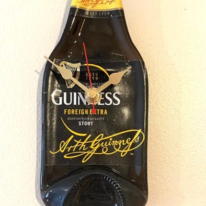 May include: A black Guinness beer bottle clock with gold hands and the text "ESTD 1759", "GUINNESS", "FOREIGN EXTRA", "DISTINCTIVE QUALITY STOUT", and "Arthur Guinness" in gold lettering.