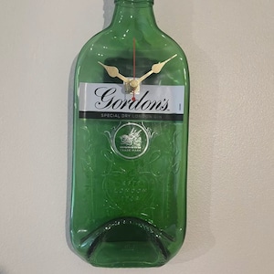 以下が含まれることがあります： 時計の文字盤と針が付いた緑色のガラス瓶。瓶には「Gordon's Special Dry London Gin」とライオンの紋章が描かれたラベルが貼られています。