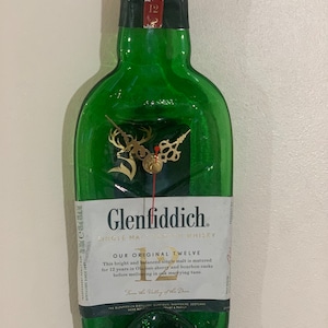 May include: A green glass clock made from a repurposed Glenfiddich whisky bottle. The clock face features a gold deer emblem and clock hands. The label reads "Glenfiddich Single Malt Scotch Whisky" and "Our Original Twelve".