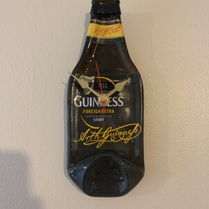 May include: A black Guinness beer bottle clock with gold hands and a black face. The clock face has the Guinness logo and the text "ESTD 1778", "FOREIGN EXTRA", "DISTINCTIVE QUALITY", "STOUT", and "Arthur Guinness".