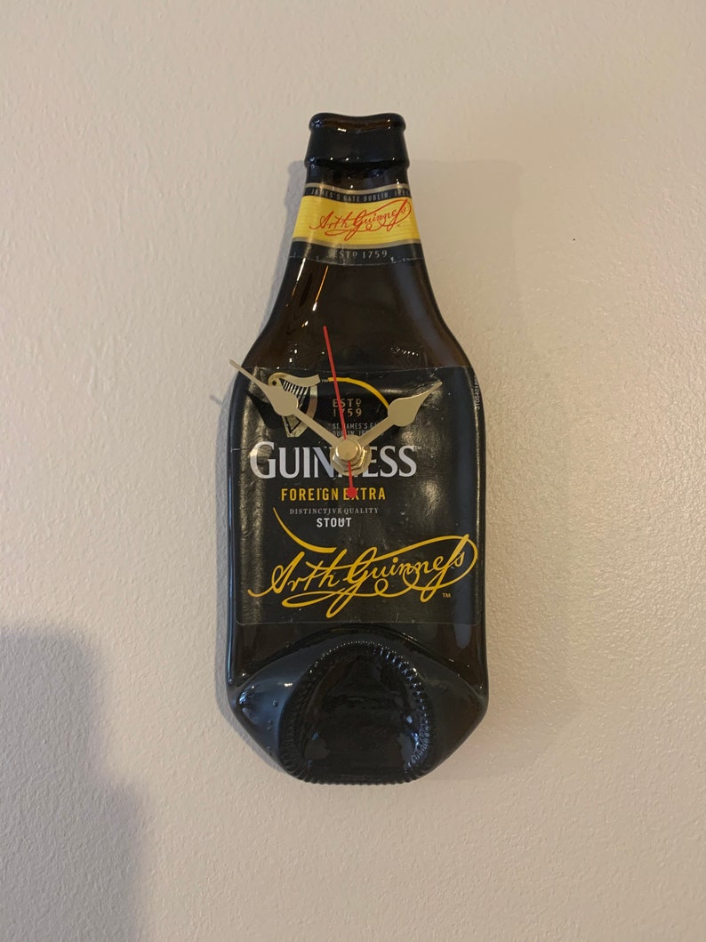 May include: A black Guinness beer bottle clock with gold hands and a black face. The clock face has the Guinness logo and the text "ESTD 1778", "FOREIGN EXTRA", "DISTINCTIVE QUALITY", "STOUT", and "Arthur Guinness".
