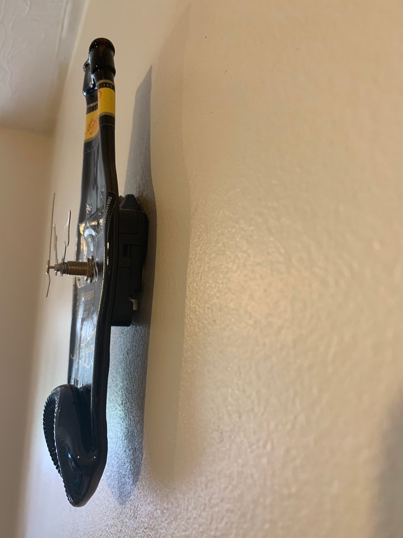 May include: A black wine bottle clock mounted on a white wall. The clock hands are visible and the bottle is positioned vertically.