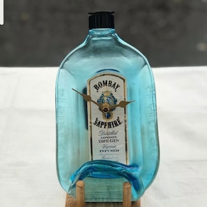 May include: A blue glass Bombay Sapphire gin bottle repurposed into a clock with gold hands and a wooden stand.