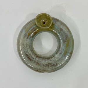 Könnte beinhalten: Ein Keramikring mit einer kleinen runden Öffnung und einer kleineren runden Öffnung oben. Der Ring ist in einem hellgrünen und braunen Farbton glasiert.