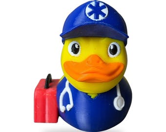 Könnte beinhalten: Eine gelbe Gummiente als medizinische Fachkraft verkleidet, mit einer blauen Mütze mit weißem Stern des Lebens-Symbol, einem blauen Hemd und einem weißen Stethoskop. Eine kleine rote medizinische Tasche ist an der Seite befestigt.