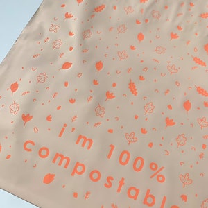 May include: A light brown compostable bag with a white background and a repeating pattern of orange leaves and other shapes. The bag has the text "i'm 100% compostable" printed in orange.
