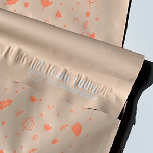 May include: A close-up of a light brown mailing bag with a white print that says "I am 100% Oxo-biodegradable". The bag has a pattern of small orange leaves and flowers.