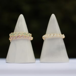 May include: Two gold wire rings with different coloured stones. The ring on the left has pink and green stones. The ring on the right has white stones.