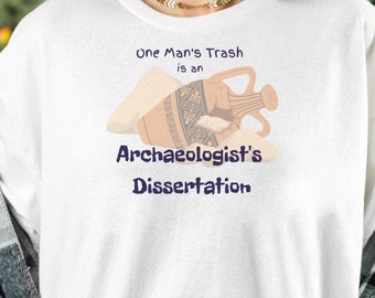 May include: White long-sleeve t-shirt with a graphic of a broken clay pot and the text "One Man's Trash is an Archeologist's Dissertation."