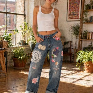 Pode incluir: Jeans de ganga clara com patches decorativos em vários desenhos florais e geométricos. Os jeans têm um corte descontraído e são combinados com uma regata branca e tênis brancos. Os patches incluem renda e aplicações de tecido.