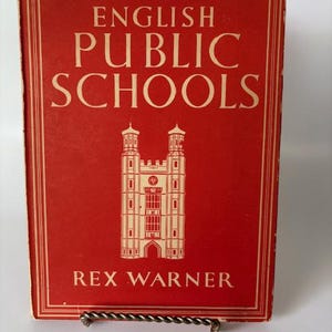 Könnte beinhalten: Ein rotes Buch mit dem Titel "English Public Schools" von Rex Warner. Das Cover zeigt weißen Text und eine detaillierte Illustration eines Gebäudes. Das Buch wird auf einem dekorativen Metallständer präsentiert.