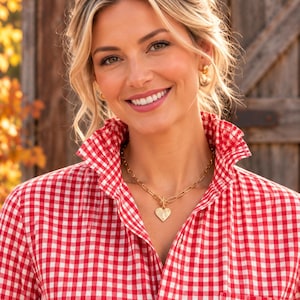May include: A gold-toned necklace featuring a textured heart-shaped pendant suspended from a chunky oval link chain. The necklace is worn with a red and white gingham button-down shirt that has a high collar and a single visible white button.
