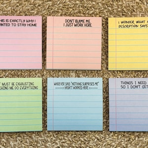 May include: Six colourful sticky note pads with humorous text. The pads are pink, peach, yellow, green, blue, and lavender. Each pad has lines and a different phrase, such as "This is exactly why I wanted to stay home."