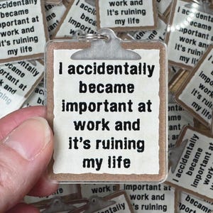 May include: A clear acrylic keychain shaped like a clipboard with a silver metal ring. The paper insert features the black printed text: I accidentally became important at work and it's ruining my life. The design mimics a standard office clipboard.