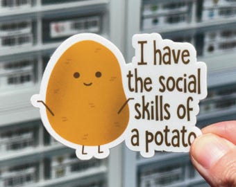 May include: A die-cut sticker featuring a cartoon potato with a simple face and thin arms. The potato is golden brown with small dark markings. To the right, brown text reads, I have the social skills of a potato, in a rounded, sans-serif font.