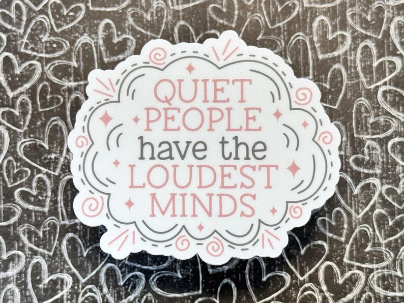 May include: A die-cut sticker with a white background featuring the text "QUIET PEOPLE have the LOUDEST MINDS" in pink and gray lettering. The design is enclosed in a decorative gray and pink scalloped border with small star and swirl accents.