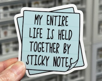 Peut inclure: Un autocollant carré bleu clair en forme de post-it avec une bordure blanche. L'autocollant présente un texte manuscrit noir qui dit : MY ENTIRE LIFE IS HELD TOGETHER BY STICKY NOTES. Le design inclut des lignes horizontales et un coin replié.
