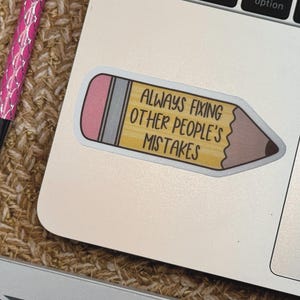 Puede incluir: Una pegatina con forma de l&aacute;piz con cuerpo amarillo, goma de borrar rosa y punta marr&oacute;n oscuro. La pegatina presenta el texto negro "ALWAYS FIXING OTHER PEOPLE'S MISTAKES" impreso claramente en el centro del cuerpo amarillo del l&aacute;piz.