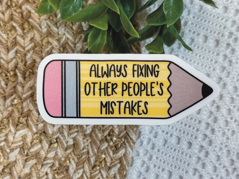 Puede incluir: Una pegatina con forma de l&aacute;piz que incluye una goma rosa, una virola plateada y un cuerpo amarillo con el texto negro ALWAYS FIXING OTHER PEOPLE'S MISTAKES. La punta del l&aacute;piz es marr&oacute;n con una mina negra y tiene un borde blanco.