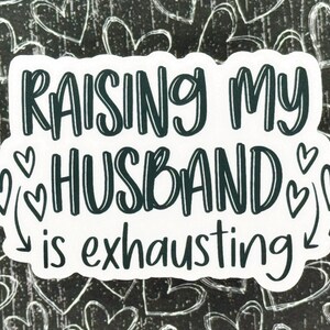 May include: White sticker with black text that reads "Raising my husband is exhausting" with hearts around the word "husband".