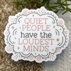May include: A white die-cut sticker with a decorative scalloped border in grey and pink. The text reads QUIET PEOPLE have the LOUDEST MINDS in a mix of pink and grey lettering, accented with small pink stars and swirling line details.