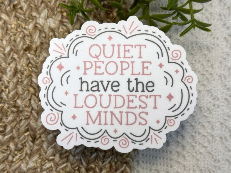 May include: A white die-cut sticker with a decorative scalloped border in grey and pink. The text reads QUIET PEOPLE have the LOUDEST MINDS in a mix of pink and grey lettering, accented with small pink stars and swirling line details.