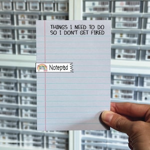 May include: A white rectangular notepad with horizontal blue lines and a vertical red margin line. The top of the page features the black printed text: THINGS I NEED TO DO SO I DON'T GET FIRED. A small logo label reads The Perky Pencil Notepad.