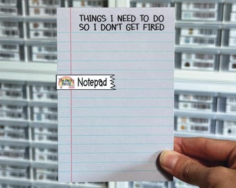 Op de afbeelding: Een wit rechthoekig notitieblok met horizontale blauwe lijnen en een verticale rode kantlijn. Bovenaan de pagina staat de zwarte tekst: THINGS I NEED TO DO SO I DON'T GET FIRED. Een klein logolabel bevat de tekst The Perky Pencil Notepad.