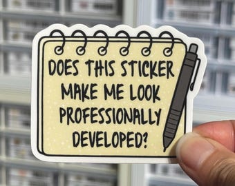 Può includere: Un adesivo fustellato a forma di blocco note a spirale con sfondo giallo pallido e un'illustrazione di una penna nera. Il testo recita: DOES THIS STICKER MAKE ME LOOK PROFESSIONALLY DEVELOPED? Il design presenta un bordo bianco e contorni neri.