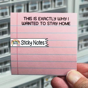 May include: A square pink sticky note with blue horizontal lines and a vertical red margin line. The text printed in black at the top reads, THIS IS EXACTLY WHY I WANTED TO STAY HOME. A logo with a rainbow and the text The Perky Pencil Sticky Notes is visible.