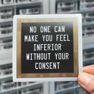 May include: A white sticker with a brown wooden frame and black text that reads "No one can make you feel inferior without your consent".
