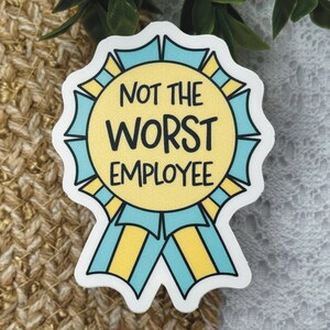 May include: A sticker with a yellow circle and blue ribbons, featuring the text "NOT THE WORST EMPLOYEE" in black. The sticker has a white border and is set against a textured background.