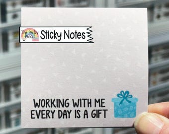 May include: A square, light-colored sticky note featuring a subtle, pale triangular pattern. The text reads "The Perky Pencil Sticky Notes" at the top and "WORKING WITH ME EVERY DAY IS A GIFT" at the bottom, accompanied by a blue gift box icon.