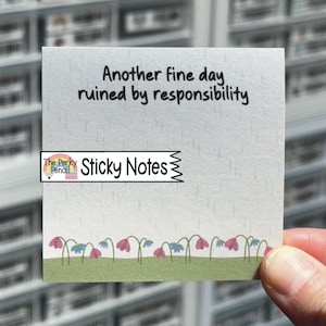 May include: A square sticky note featuring the black text Another fine day ruined by responsibility, a light gray background with subtle rain lines, and a bottom border of green grass with small pink and blue flowers. A logo reads The Perky Pencil.