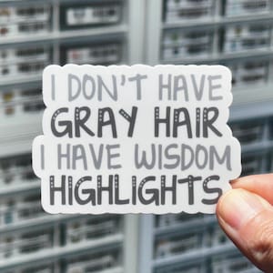May include: White sticker with black and gray text that reads "I don't have gray hair I have wisdom highlights".