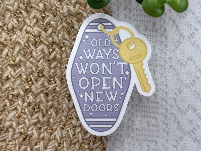 Pu&ograve; includere: Un adesivo a forma di portachiavi da motel color lavanda con una chiave gialla attaccata in alto. L'adesivo mostra il testo bianco OLD WAYS WON'T OPEN NEW DOORS, accentuato da piccole stelle a quattro punte all'interno del bordo viola.
