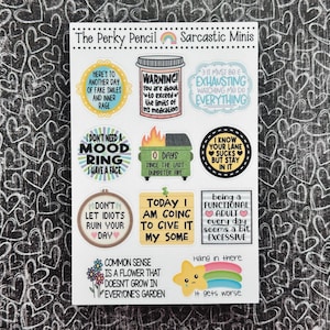 May include: A sheet of colorful stickers with sarcastic sayings. The stickers are round, square, and rectangular. Some of the sayings include "I don't need a mood ring, I have a face", "Here's to another day of fake smiles and inner rage", and "Today I am going to give it my some".