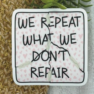 May include: White sticker with a cracked design. The sticker has a pink background with small pink hearts. The text on the sticker reads "We repeat what we don't repair."