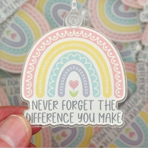 May include: A rainbow-colored acrylic keychain with a white background and the text "Never forget the difference you make".
