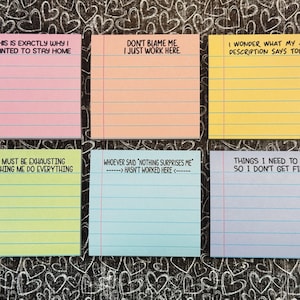May include: Six colourful sticky notes with humorous phrases in black text. The notes are pink, peach, yellow, green, blue, and lavender. The background is a black surface with white heart doodles.