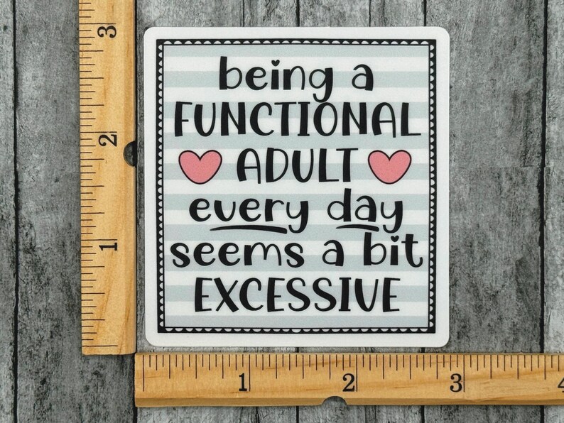 May include: A square sticker with a light blue and white horizontal striped background and a black border. The text reads being a FUNCTIONAL ADULT every day seems a bit EXCESSIVE with two pink hearts. A wooden ruler shows it is 3 inches wide.